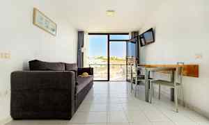 Olohuone, jossa on tumma sohva, ruokapöytä tuoleineen ja parveke, josta on näkymä. (Tekoälyn luoma teksti)