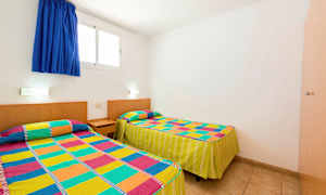 Huone, jossa on kaksi yhden hengen vuodetta, joissa on värikkäät kuviolliset päiväpeitteet. (Tekoälyn luoma teksti)