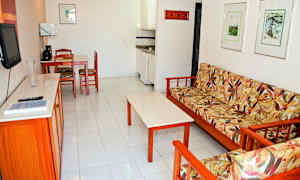 Olohuone, jossa kukkakuvioinen sohva, sohvapöytä, keittiönurkkaus ja ruokapöytä tuoleineen. (Tekoälyn luoma teksti)