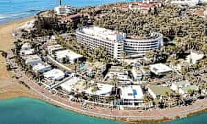 Ilmakuva rannikkokaupungista, jossa hotelleja, palmuja ja hiekkaranta. (Tekoälyn luoma teksti)