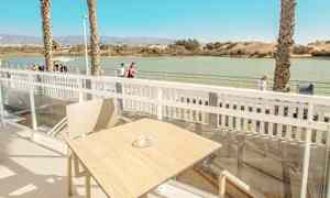 Näkymä terassilta, jolla on pöytä ja tuoli. Taustalla näkyy vettä ja kävelytie. (Tekoälyn luoma teksti)