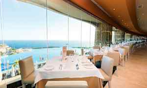 Ravintola, jossa on katettuja pöytiä ja näkymä merelle suurten lasi-ikkunoiden läpi. (Tekoälyn luoma teksti)