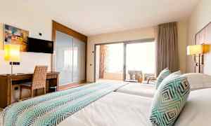 Hotellihuoneen kuva, jossa on kaksi vuodetta, työpöytä, televisio ja parveke tuoleineen. (Tekoälyn luoma teksti)