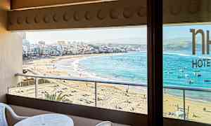 Näkymä parvekkeelta hiekkarannalle ja kaupunkiin, jossa on kirkkaan sininen meri. (Tekoälyn luoma teksti)