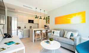 Modernin keittiön sisustus, jossa integroitu oleskelualue, harmaa sohva ja värikäs taideteos. (Tekoälyn luoma teksti)