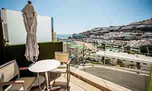 Parveke, jolta on näkymä rannalle ja vuorille, joissa on rakennuksia. (Tekoälyn luoma teksti)