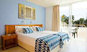 Hotellihuone, jossa on kaksi erillistä sänkyä, sininen seinä ja lasiovi, joka johtaa parvekkeelle. (Tekoälyn luoma teksti)