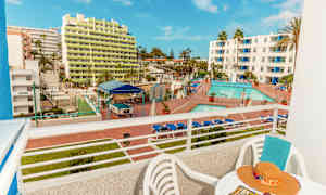 Näkymä parvekkeelta hotellialueelle, jossa on uima-allas ja aurinkotuolit sekä rakennuksia taustalla. (Tekoälyn luoma teksti)