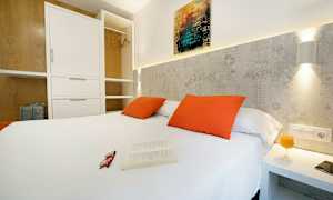 Makuuhuone, jossa valkoinen parisänky, oranssit tyynyt ja avoin vaatekaappi. (Tekoälyn luoma teksti)