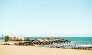 Hiekkaranta, näkymä kallioalueelle ja pienvenesatamaan meren äärellä. (Tekoälyn luoma teksti)