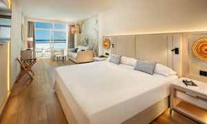 Hotellihuone, jossa suuri sänky, sohva ja näkymä merelle ikkunan läpi. (Tekoälyn luoma teksti)