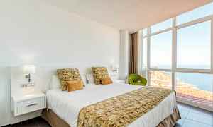 Hotellihuone, jossa on pedattu sänky, suuret ikkunat ja näkymä merelle. (Tekoälyn luoma teksti)