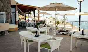 Terassi, jossa pöytiä ja tuoleja sekä näköala merelle. (Tekoälyn luoma teksti)