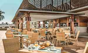 Ulkokahvila-alue, jossa on puupöydät, tuolit ja katto, koristeltu kasveilla ja pöytäliinoilla, tarjoaa ruokaa ja juomia. (Tekoälyn luoma teksti)