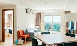 Hotellihuone, jossa oleskelutila, ruokapöytä ja merinäköala parvekkeelta. (Tekoälyn luoma teksti)