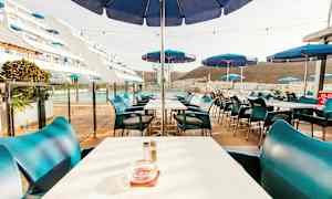 Kuva ulkoilmaravintolasta, jossa on pöytiä ja sinisiä aurinkovarjoja. (Tekoälyn luoma teksti)