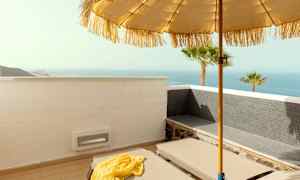 Aurinkotuoli terassilla, näkymä merelle, aurinkovarjo ja palmuja. (Tekoälyn luoma teksti)