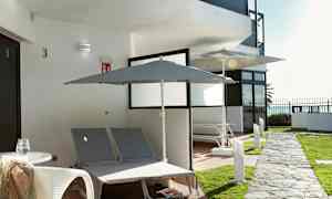 Ulkotila, jossa kaksi aurinkotuolia ja aurinkovarjoja rakennuksen luona. (Tekoälyn luoma teksti)