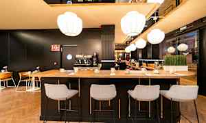 Modernin kahvilan tai baarin sisustus, jossa on korkea pöytä ja tuolit, kahvikone ja valaistus. (Tekoälyn luoma teksti)