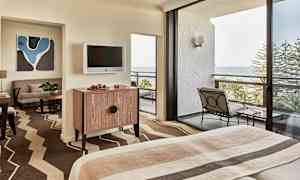 Hotellihuone, jossa sänky, huonekaluja ja parveke merinäköalalla. (Tekoälyn luoma teksti)