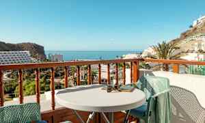 Näkymä parvekkeelta, jossa pöytä ja tuolit, kohti merta ja ympäröiviä rakennuksia. (Tekoälyn luoma teksti)