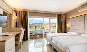 Hotellihuone, jossa kaksi yhden hengen sänkyä, kirjoituspöytä ja näkymä maisemaan lasioven kautta. (Tekoälyn luoma teksti)