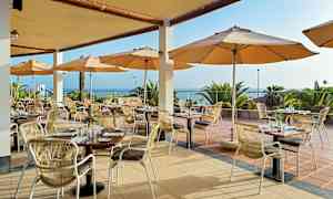 Ravintola, jossa ulkoterassi, pöytiä ja tuoleja varjojen alla, näkymä merelle. (Tekoälyn luoma teksti)