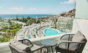 Näkymä parvekkeelta hotellille, jossa on suuri uima-allas, ympäröivä palmuja ja meri taustalla. (Tekoälyn luoma teksti)