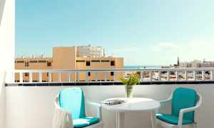 Parveke, jossa on kaksi tuolia, pöytä ja näkymä rakennuksille ja merelle. (Tekoälyn luoma teksti)