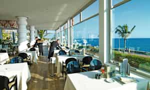 Ravintola, jossa katettuja pöytiä ja ikkunat merelle päin. (Tekoälyn luoma teksti)