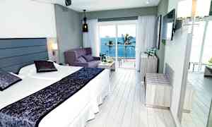 Hotellihuone, jossa on parivuode, sohva ja merinäköala suurten ikkunoiden takana. (Tekoälyn luoma teksti)