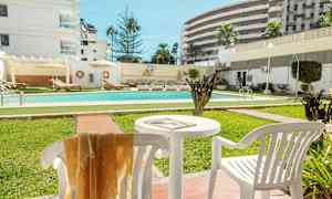 Ulkouima-allas, jota ympäröivät viheralueet ja aurinkotuolit, taustalla valkoisia rakennuksia. (Tekoälyn luoma teksti)