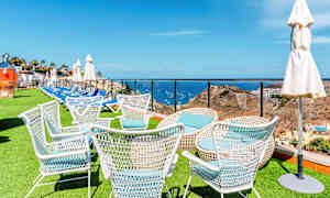 Valkoisia puutarhatuoleja nurmikolla, taustalla meri ja maisema. (Tekoälyn luoma teksti)