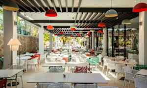 Moderni ravintola, jossa paljon värikkäitä tuoleja ja pöytiä. (Tekoälyn luoma teksti)