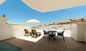 Terasilla aurinkotuoleja, varjo ja ulkokalusteet, näkymä aurinkoon ja mäenrinteeseen. (Tekoälyn luoma teksti)