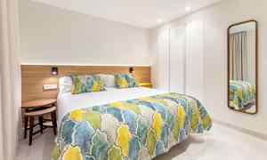 Moderni hotellihuone, jossa on värikkäillä päiväpeitteillä ja tyynyillä varustettu sänky sekä seinällä peili. (Tekoälyn luoma teksti)