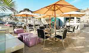 Ulkoterassi pöytien, tuolien ja aurinkovarjojen kera, jota ympäröi vuoristomaisema. (Tekoälyn luoma teksti)