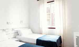 Hotellihuone, jossa on kaksi erillistä vuodetta valkoisilla lakanoilla ja sinisillä vilteillä. (Tekoälyn luoma teksti)