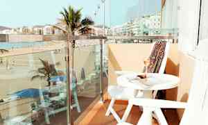 Parveke, jolta näkyy ranta ja palmuja, pöytä ja tuolit. (Tekoälyn luoma teksti)