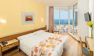 Hotellihuone, jossa kaksi sänkyä, keltainen sisustus ja parveke, jolta on näkymä merelle. (Tekoälyn luoma teksti)