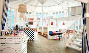 Sisäbaari, jossa on valkoisia ja punaisia huonekaluja sekä suuret ikkunat. (Tekoälyn luoma teksti)