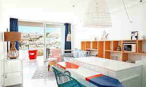 Valoisasti sisustettu huoneisto, jossa värikkäitä huonekaluja ja näkymä vuorelle parvekkeen oven kautta. (Tekoälyn luoma teksti)