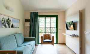 Olohuone, jossa sininen sohva, rottinkituoli ja seinälle asennettu televisio. (Tekoälyn luoma teksti)