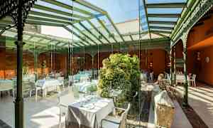 Sisätilaravintola, jossa lasiseinät ja katto, koristeltu vihreillä kasveilla ja pöydillä. (Tekoälyn luoma teksti)