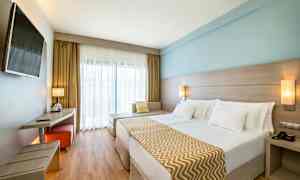 Kahden hengen huone, jossa on moderni sisustus, vaaleat värit ja suuri sänky. (Tekoälyn luoma teksti)