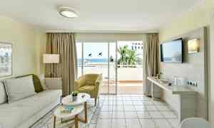 Olohuone, jossa on vaaleat huonekalut ja suuret lasiovet, jotka johtavat parvekkeelle merinäköalalla. (Tekoälyn luoma teksti)