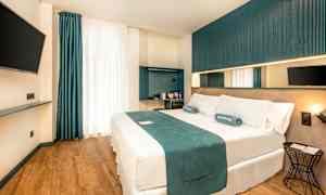 Moderni hotellihuone, jossa on parivuode, seinälle kiinnitetty televisio ja minimalistinen sisustus. (Tekoälyn luoma teksti)