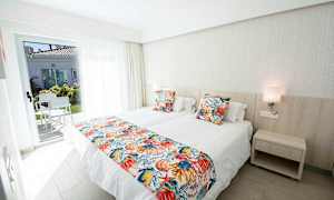 Hotellihuone, jossa on kaksi yhden hengen sänkyä, värikkäät tyynyliinat ja ovi terassille. (Tekoälyn luoma teksti)