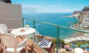 Näkymä parvekkeelta, pöytä ja kaksi tuolia, tarjoillut lasit, meri ja rannikko maisemaan. (Tekoälyn luoma teksti)