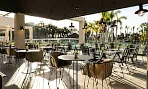 Ulkoravintola, jossa on moderneja kalusteita, palmujen ympäröimänä. (Tekoälyn luoma teksti)